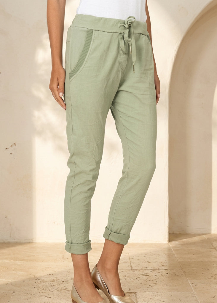A person wearing light sage green cropped drawstring pants with side pockets and rolled cuffs, paired with a white top and beige heeled sandals against a plain light background.