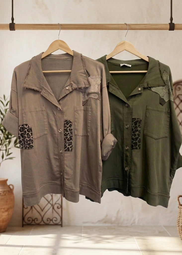 Two patchwork button-up shirts hanging on black hangers against a plain white wall. The left shirt is taupe with leopard-print and camouflage patches, and the right shirt is olive green with similar patches.