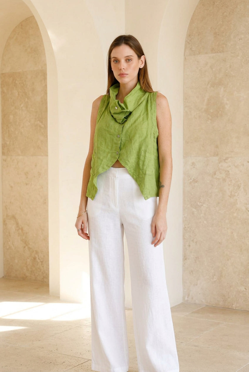 A woman modeling a sleeveless lime green linen shirt with a ruffled collar and front button detail, paired with dark blue jeans, against a plain beige background.