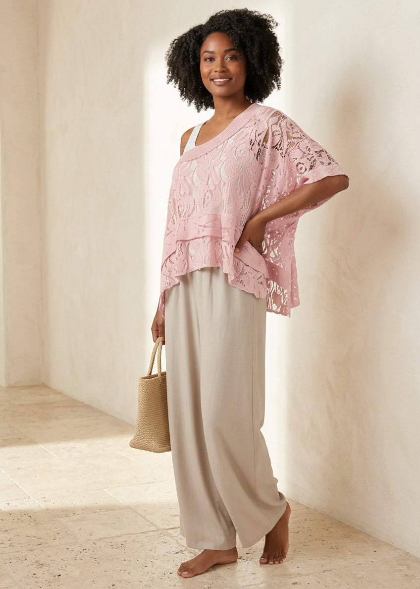 A woman modeling a light pink lace ruffled top with beige wide-leg pants, holding a beige straw tote bag against a light gray studio background.