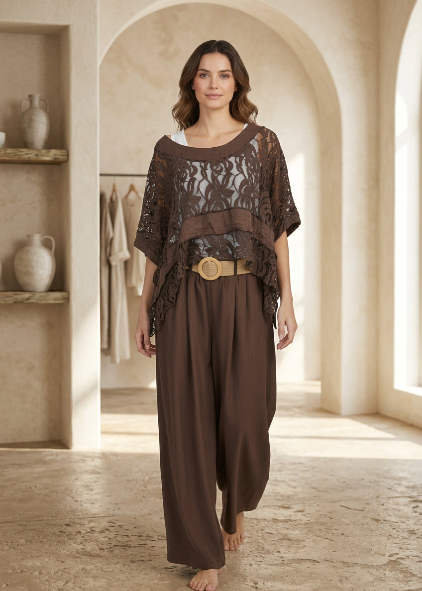 A woman modeling a brown two-piece outfit consisting of a sheer floral lace short-sleeve top and matching wide-leg pants, styled with a gold belt, against a light gray studio background.