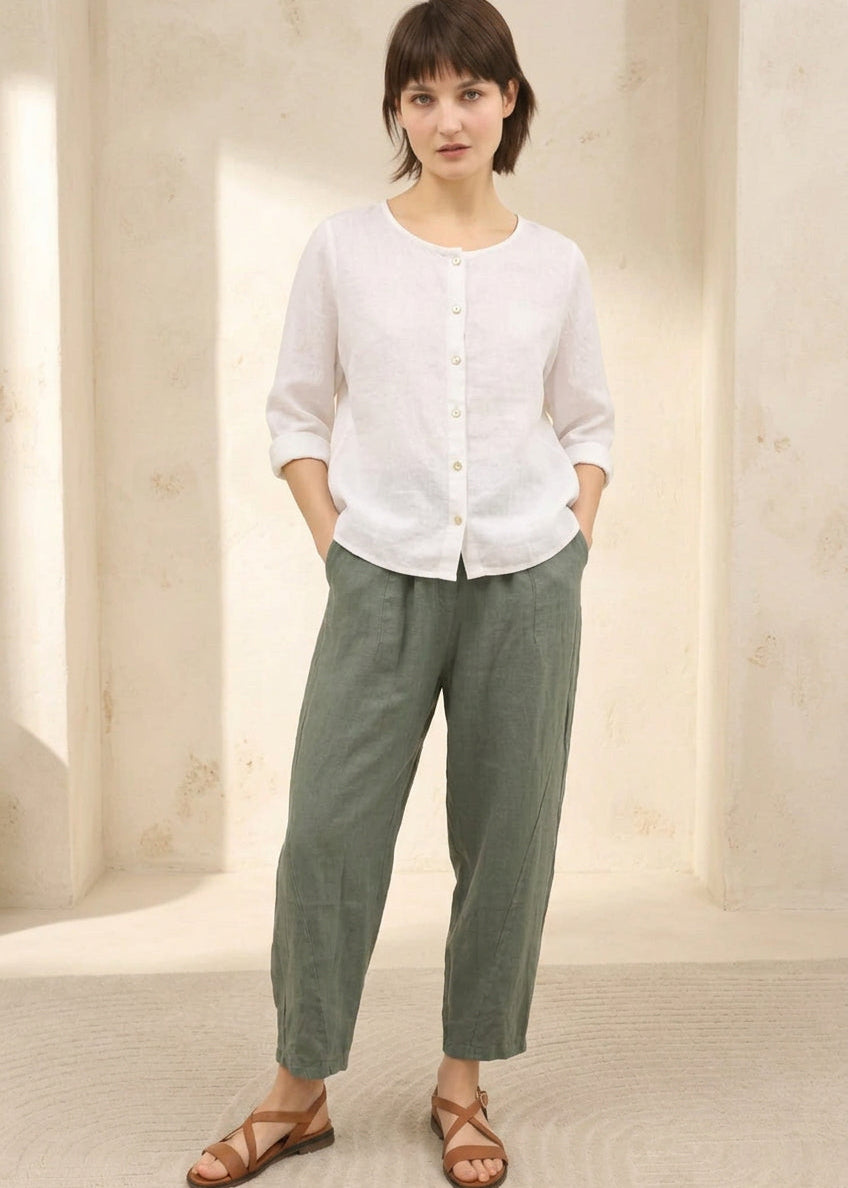 A woman modeling a three-quarter sleeve olive green top and matching olive green wide-leg cropped pants, paired with brown leather sandals, set against a warm beige architectural background.