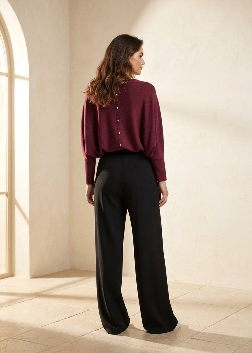 A woman shown from the back wearing a burgundy long-sleeve button-front top and black wide-leg trousers, photographed against a light gray studio background.
