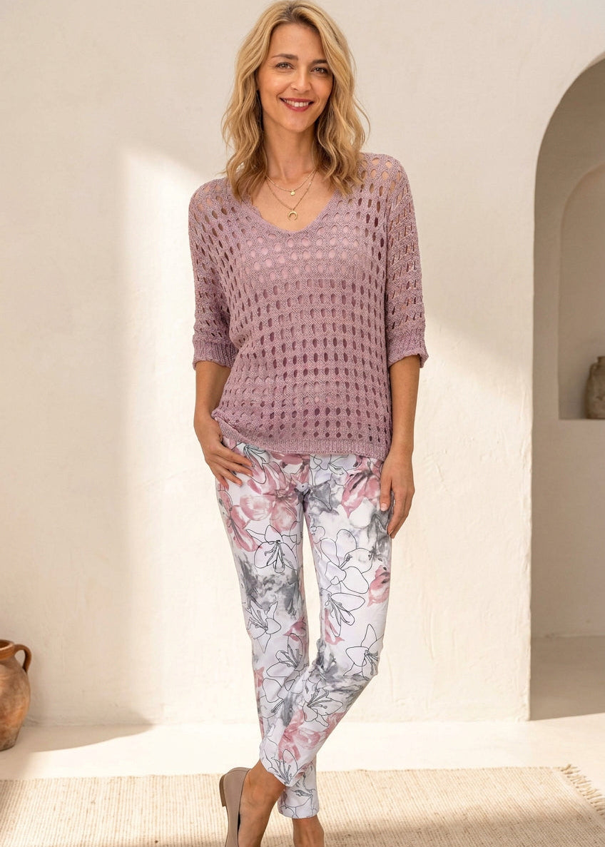 A woman modeling a dusty pink open-knit short-sleeve top paired with white leggings featuring a pink and gray floral print, standing against a plain white studio background.