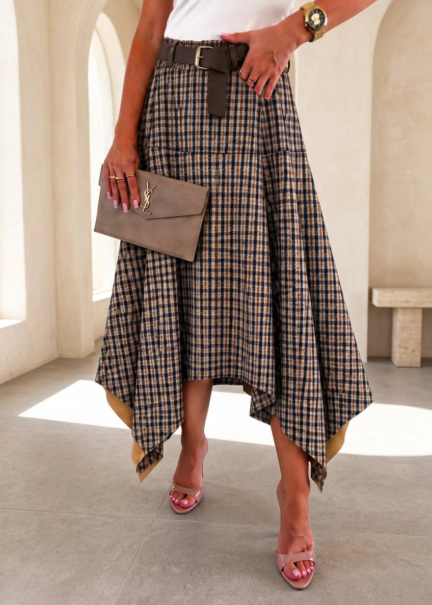 A woman models a brown, beige, and black plaid high-low midi skirt with a matching belt, paired with a white top and pink heels in a boutique setting.